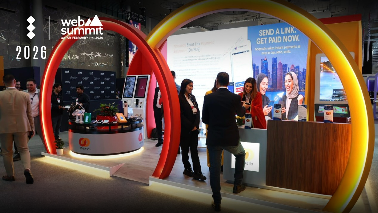 Noqoody's award-winning booth at Web Summit Qatar 2026 in Doha — large red and amber illuminated arches around a branded counter with POS devices and a 'Send a link. Get paid now.' display